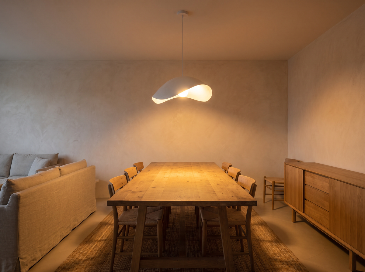 The same living-dining room with the pendant on, warm light pooling on the oak table